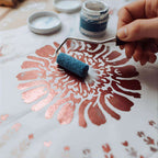 Hand using paint roller to apply rose gold floral stencil design on canvas, DIY home decor craft